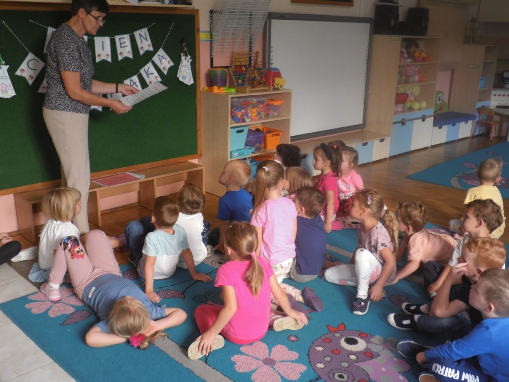 Na zdjęciu, dzieci siedzą na dywanie przed nauczycielem