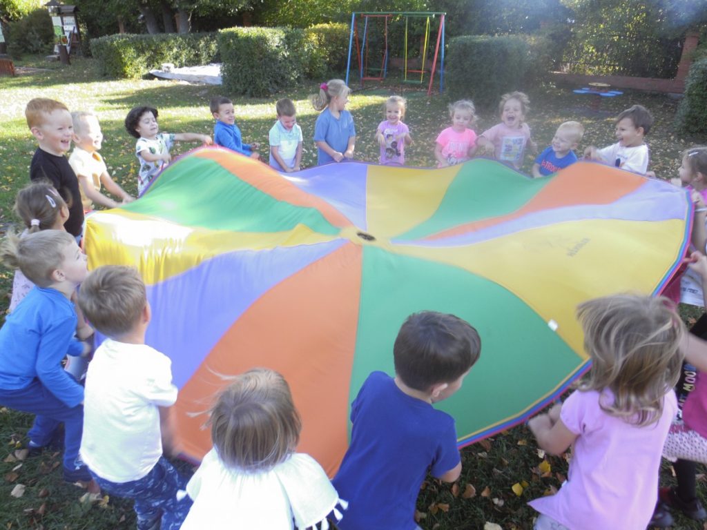 Na zdjęciu, dzieci na placu zabaw bawią się kolorową chustą