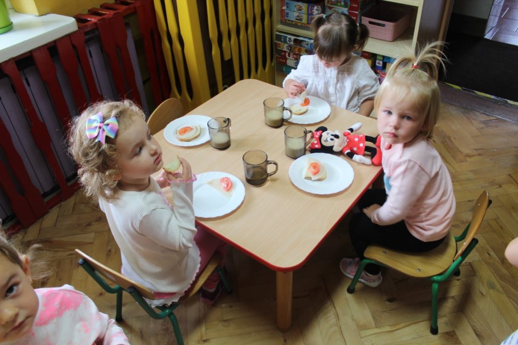 Dzieci siedzą przy stoliku i jedzą śniadanie 