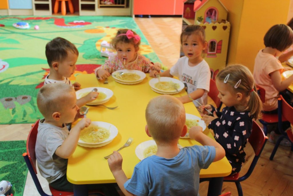 Szóstka dzieci siedzi przy stoliku i zjada rosołek
