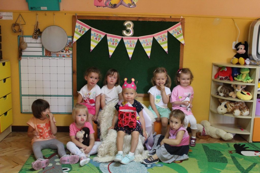 Dziewczynka siedzi w koronie a obok dziewczynki z jej grupy pozują do zdjęcia z okazji urodzin
