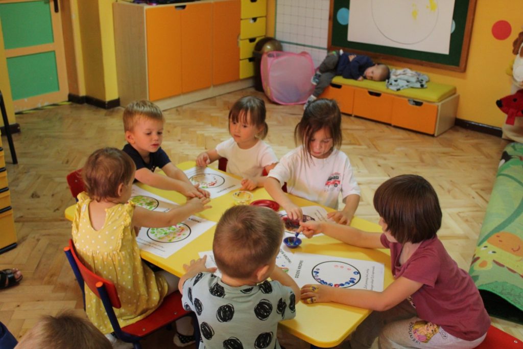 Dzieci przy stoliku malują paluszkiem kropkę w rożnych kolorach