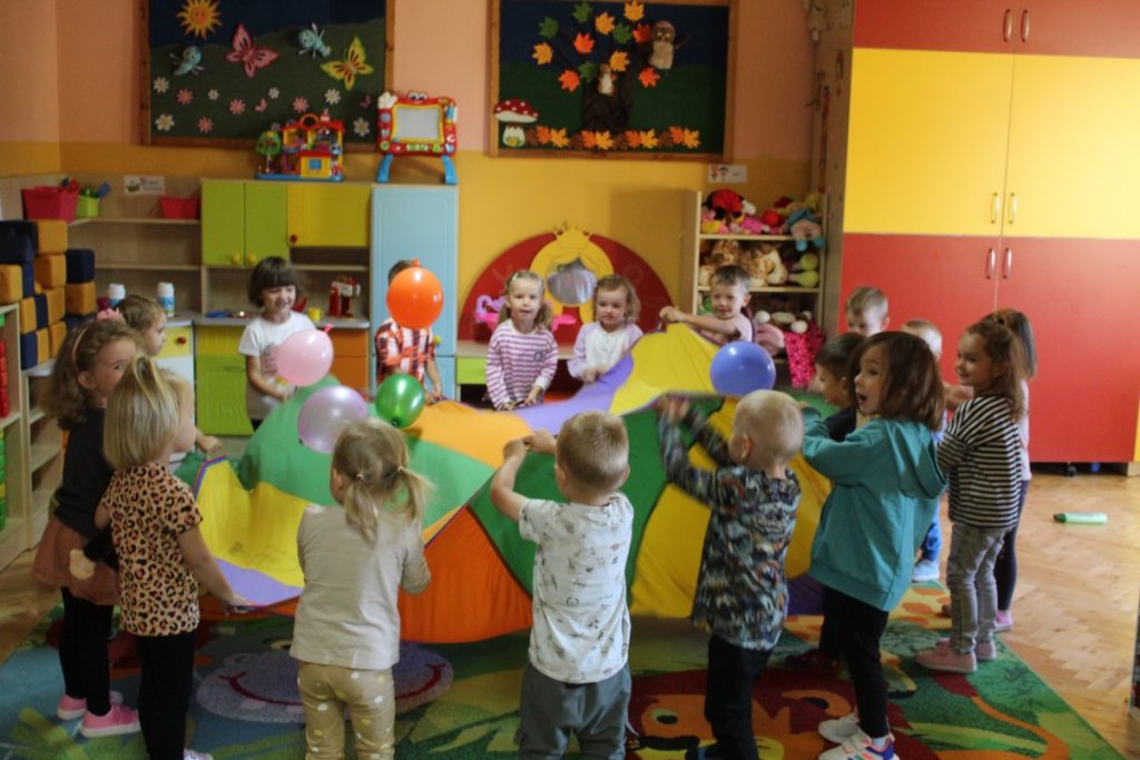 Dzieci trzymają i poruszają chustę animacyjną odbijając baloniki