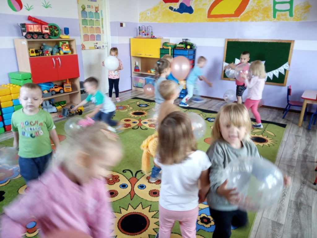 Na zdjęciu dzieci tańczą z balonami na dywanie.