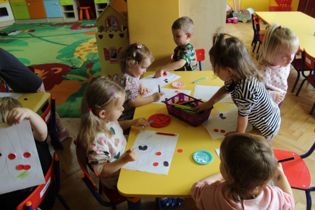 Dzieci przy stoliku układają na kartkach jabłka i śliwki z papieru