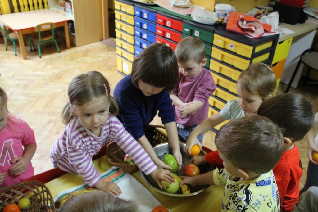 Dzieci wokół stolika na stoliku miska  z wodą . Dzieci myją owoce