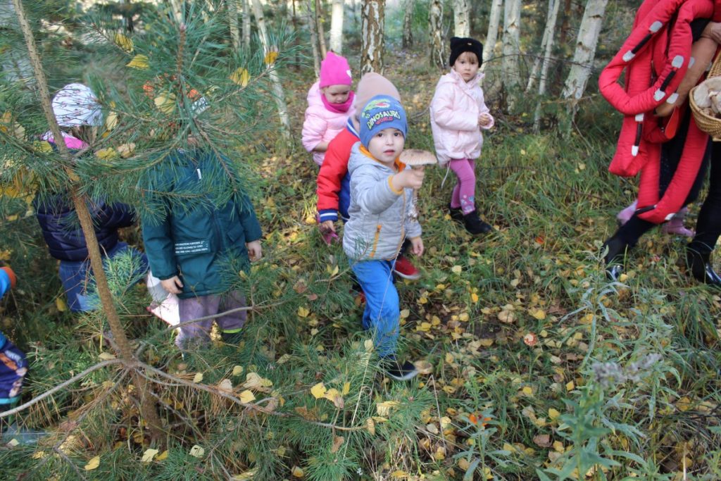 Grupka dzieci w lesie chłopiec trzyma grzyba 