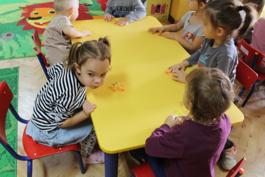 Dzieci przy stolikach dmuchają na listki 