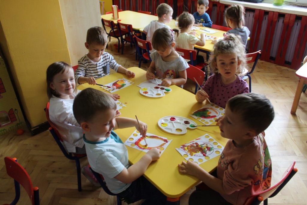 Dzieci przy stolikach malują liście papierowe na jesienne kolory