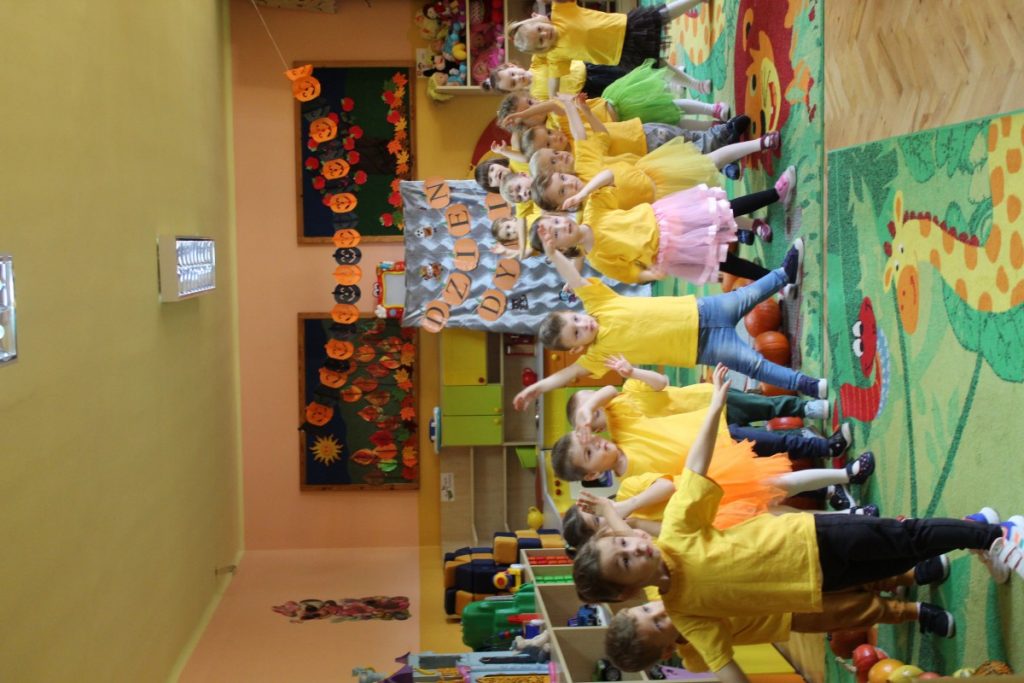 Dzieci w żółtych podkoszulkach pozują przy dyniach