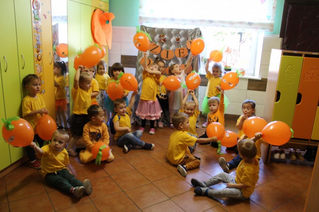 grupa dzieci w żółtych podkoszulkach z pomarańczowymi balonami pozuje do zdjęcia grupowego