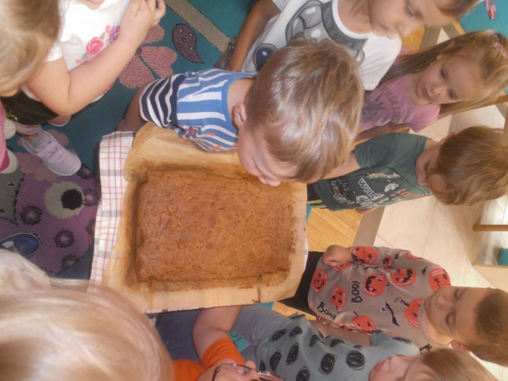 Na zdjęciu dzieci wąchają upieczone ciasto z dyni