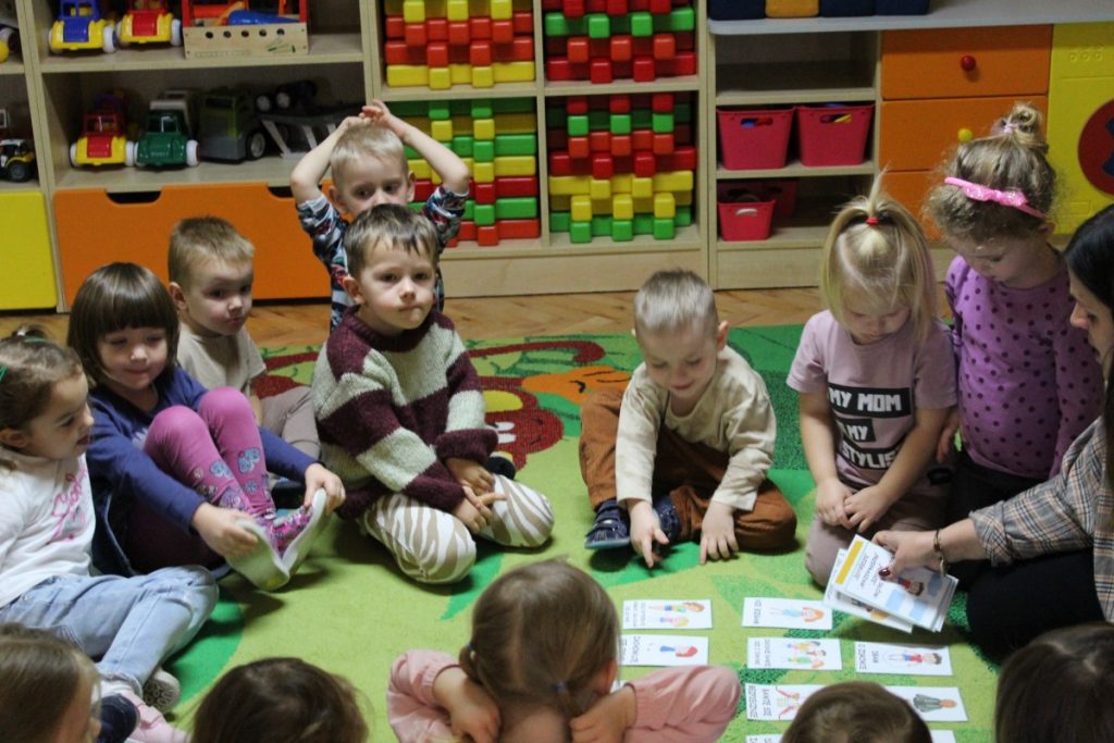 Dzieci wraz z nauczycielką siedzą
a na dywanie