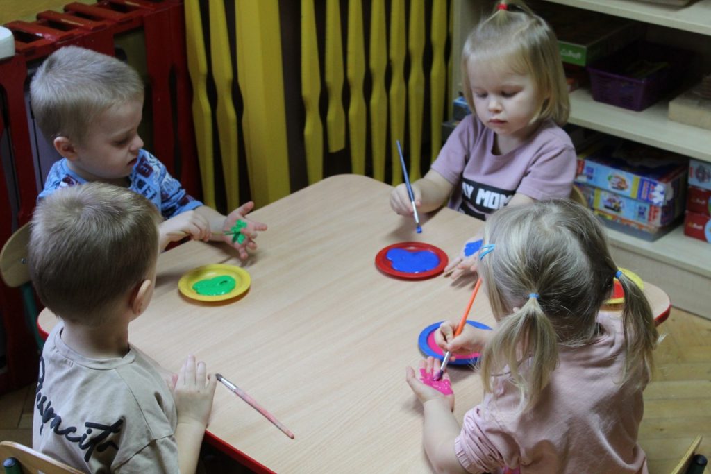Czwórka dzieci przy stoliku maluje pędzlem każde swoją dłoń