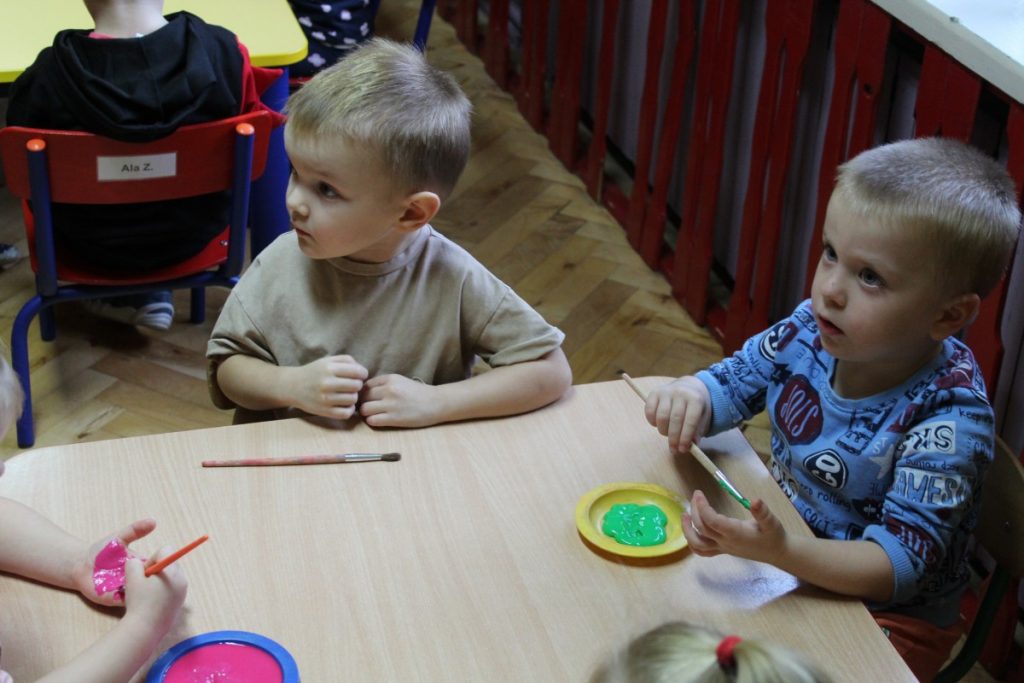 Dwójka dzieci przy stoliku maluje pędzlem każde swoją dłoń