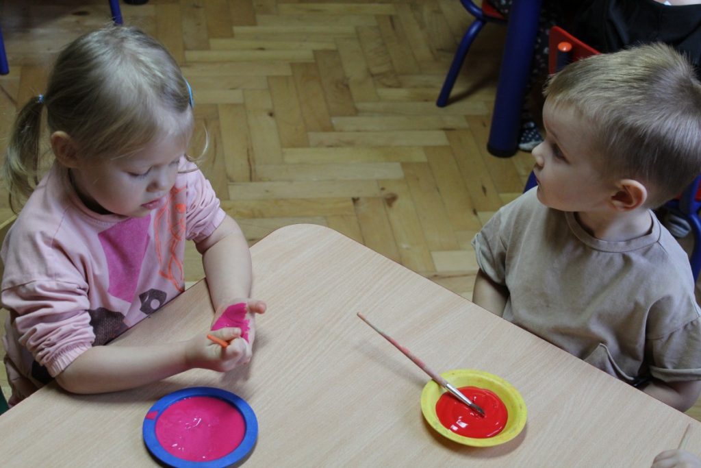 Dwójka dzieci przy stoliku maluje pędzlem każde swoją dłoń