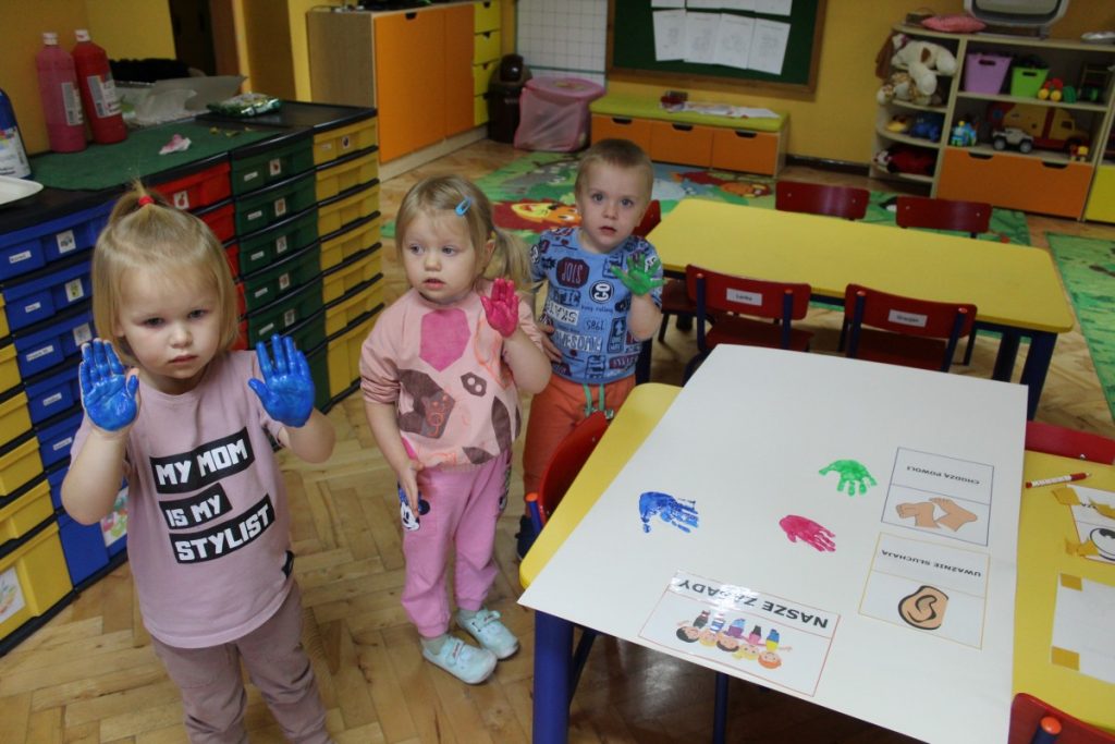 Trójka dzieci stoi i pokazuje pomalowane farbą dłonie