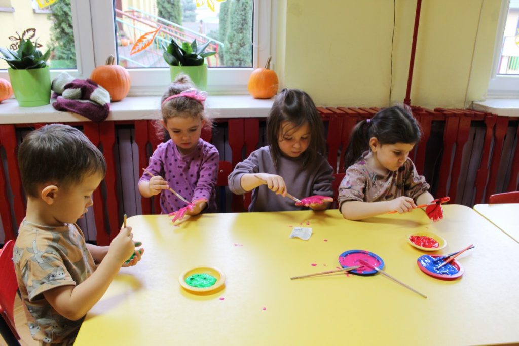 Czwórka dzieci przy stoliku maluje dłonie pędzlem