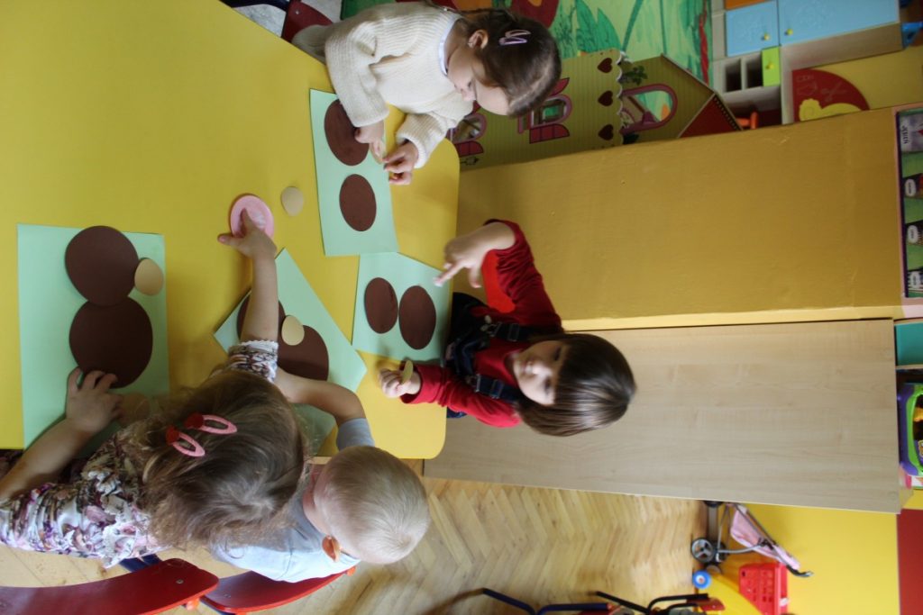 Dzieci przy stoliku układają misia z brązowych kółek