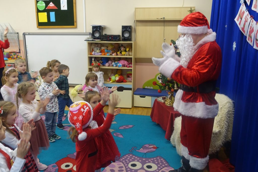 Dzieci stoją wraz z Mikołajem na
 dywanie, śpiewają piosenkę 
