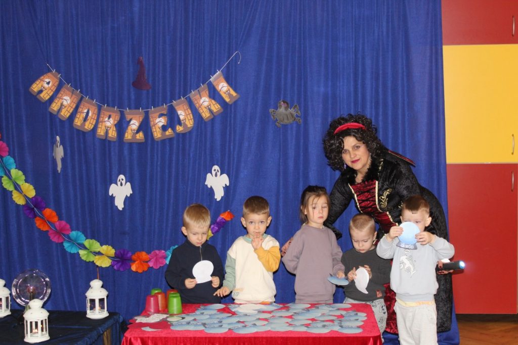 grupka dzieci przy stoliku, kobieta przebrana za czarownicę