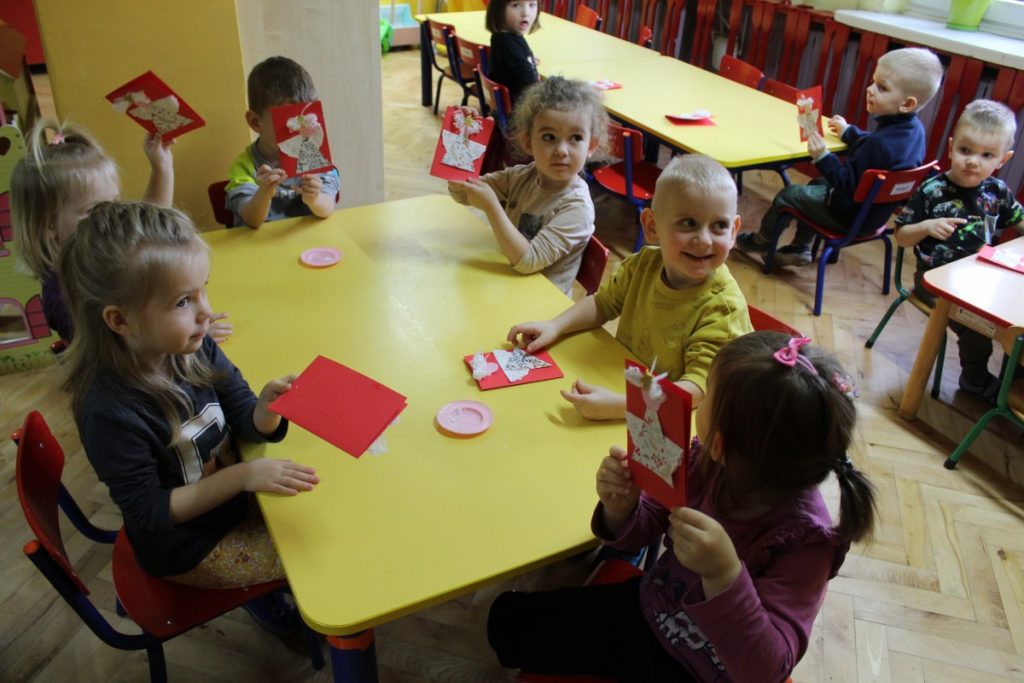 Dzieci przy stoliku siedzą i pokazują wykonane świąteczne kartki z aniołkami