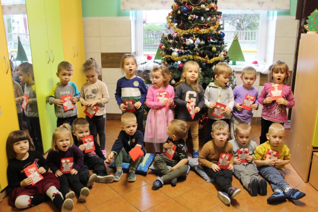 Grupa dzieci przy choince w rękach trzymają świąteczne kartki