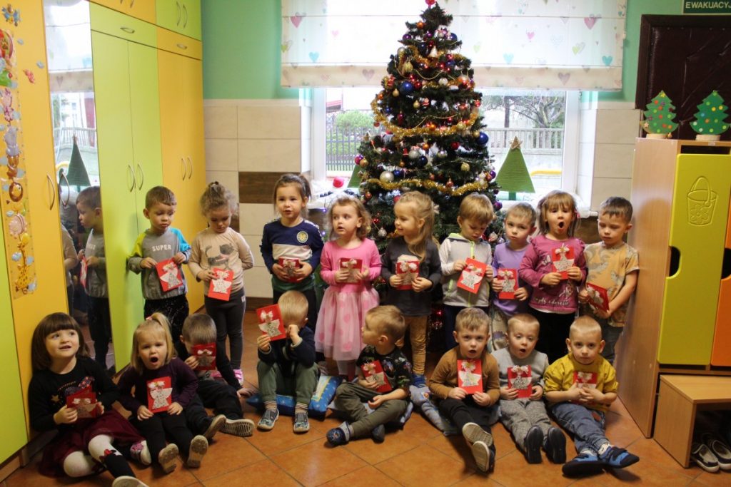 Grupa dzieci przy choince w rękach trzymają świąteczne kartki