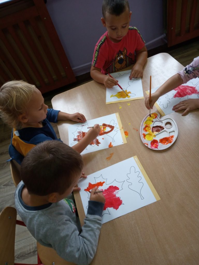 Na zdjęciu dzieci siedzą przy stoliku, malują farbami.