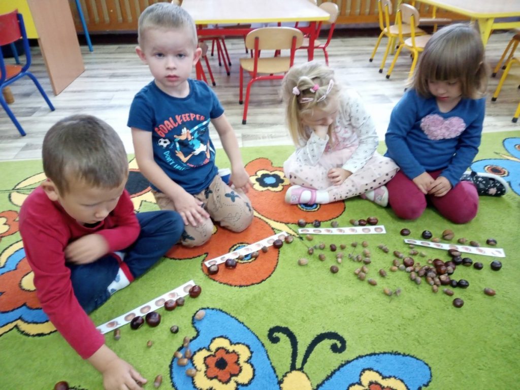 Na zdjęciu dzieci siedzą na dywanie, układają jesienne rytmy.