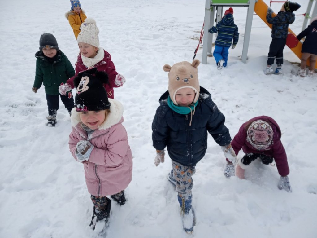 Na zdjęciu są dzieci na przedszkolnym placu zabaw, które bawią się na śniegu.