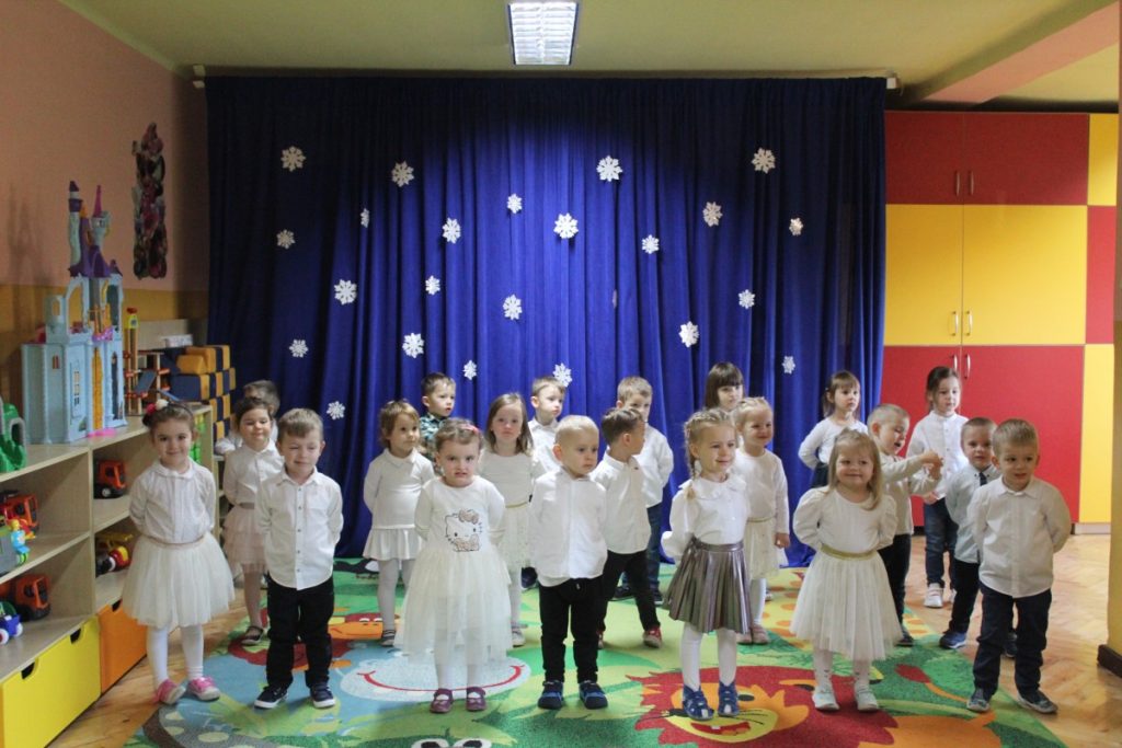 Grupa dzieci ubranych na biało na tle dekoracji granatowej z białymi gwiazdkami