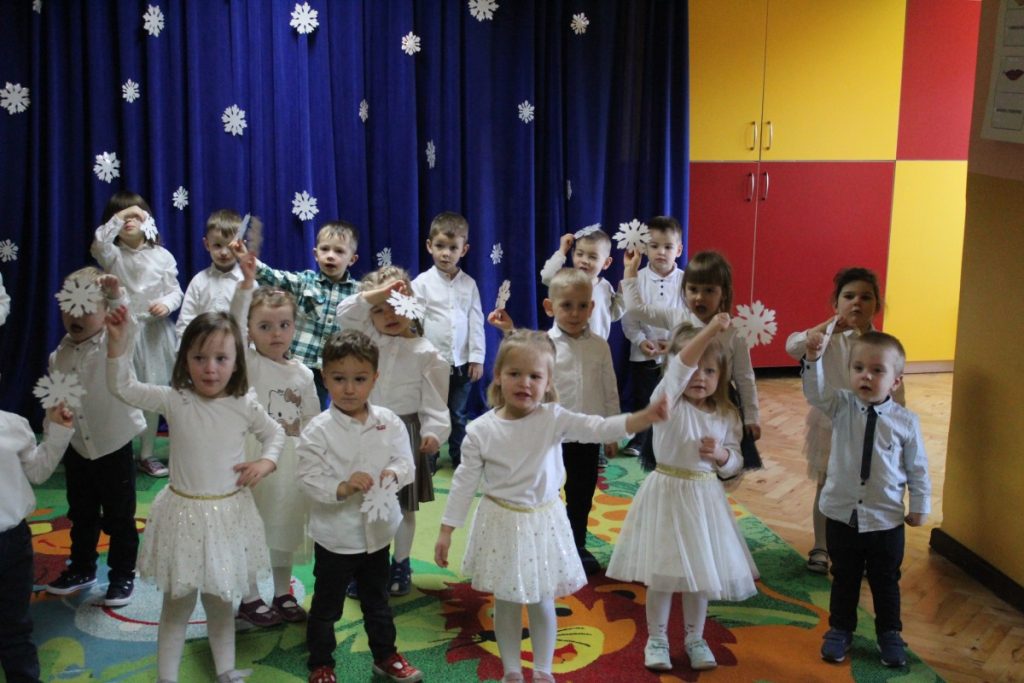 Grupa dzieci ubranych na biało na tle dekoracji granatowej z białymi gwiazdkami
