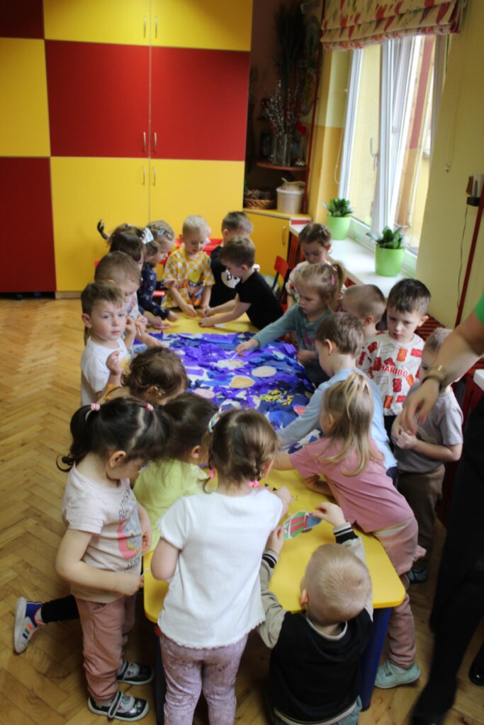 Dzieci przy stoliku układają planety na wyklejonym kartonie