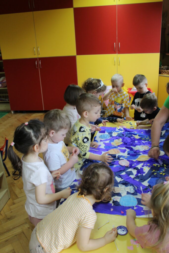 Dzieci przy stoliku układają planety na wyklejonym kartonie
