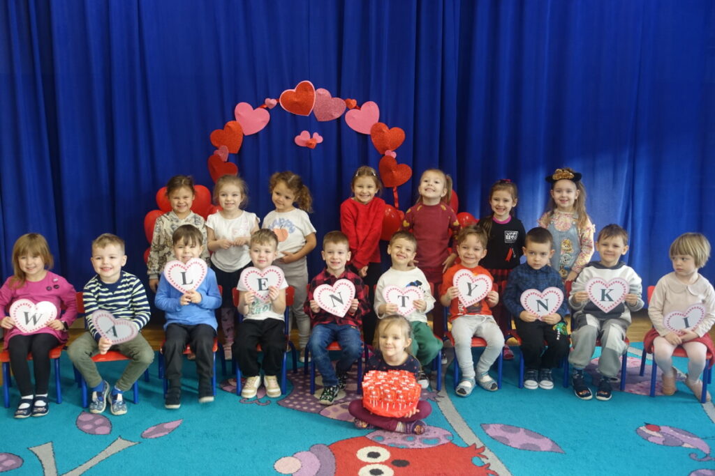 grupa dzieci siedzi na dywanie , dzieci trzymają litery, które tworzą napis Walentynki