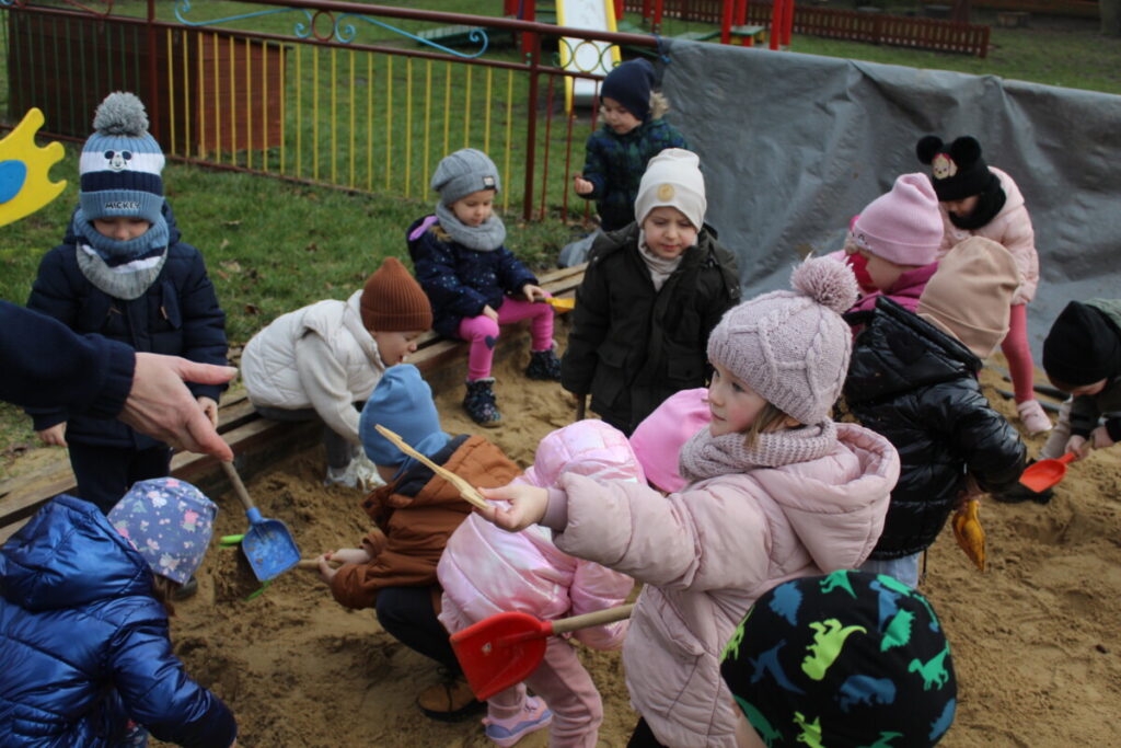 Grupka dzieci szuka w piaskownicy kości dinozaurów. Zabawa w paleontologów