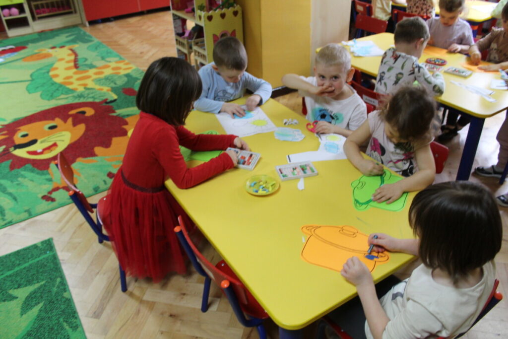 dzieci przy stoliku wyklejają z papieru bazie 