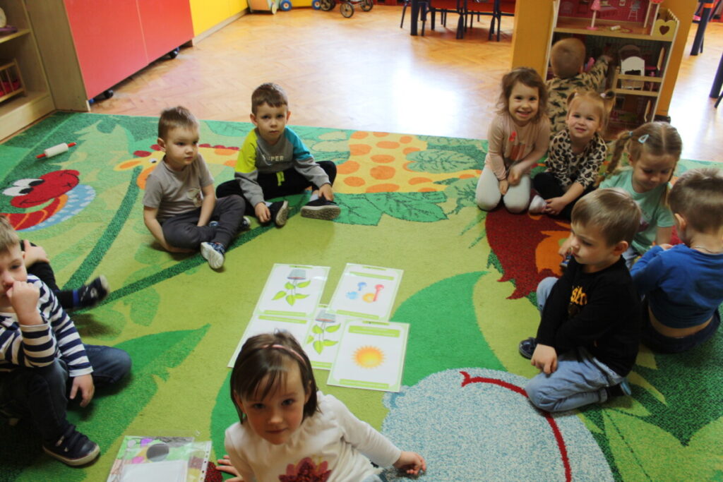 Dzieci siedzą na dywanie na środku karty dydaktyczne