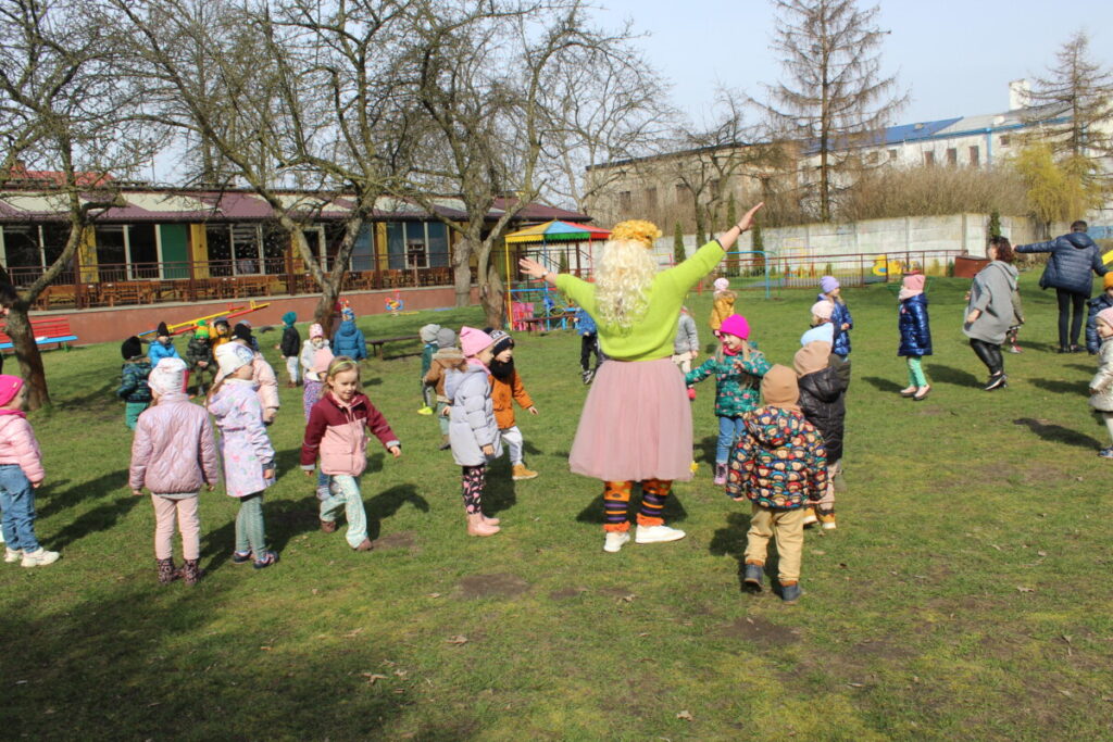 Dzieci w kole na placu zabaw w środku kobieta przebrana za wiosnę