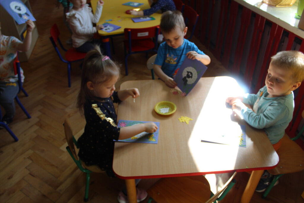 Dzieci przy stoliku układają baranka na kartce